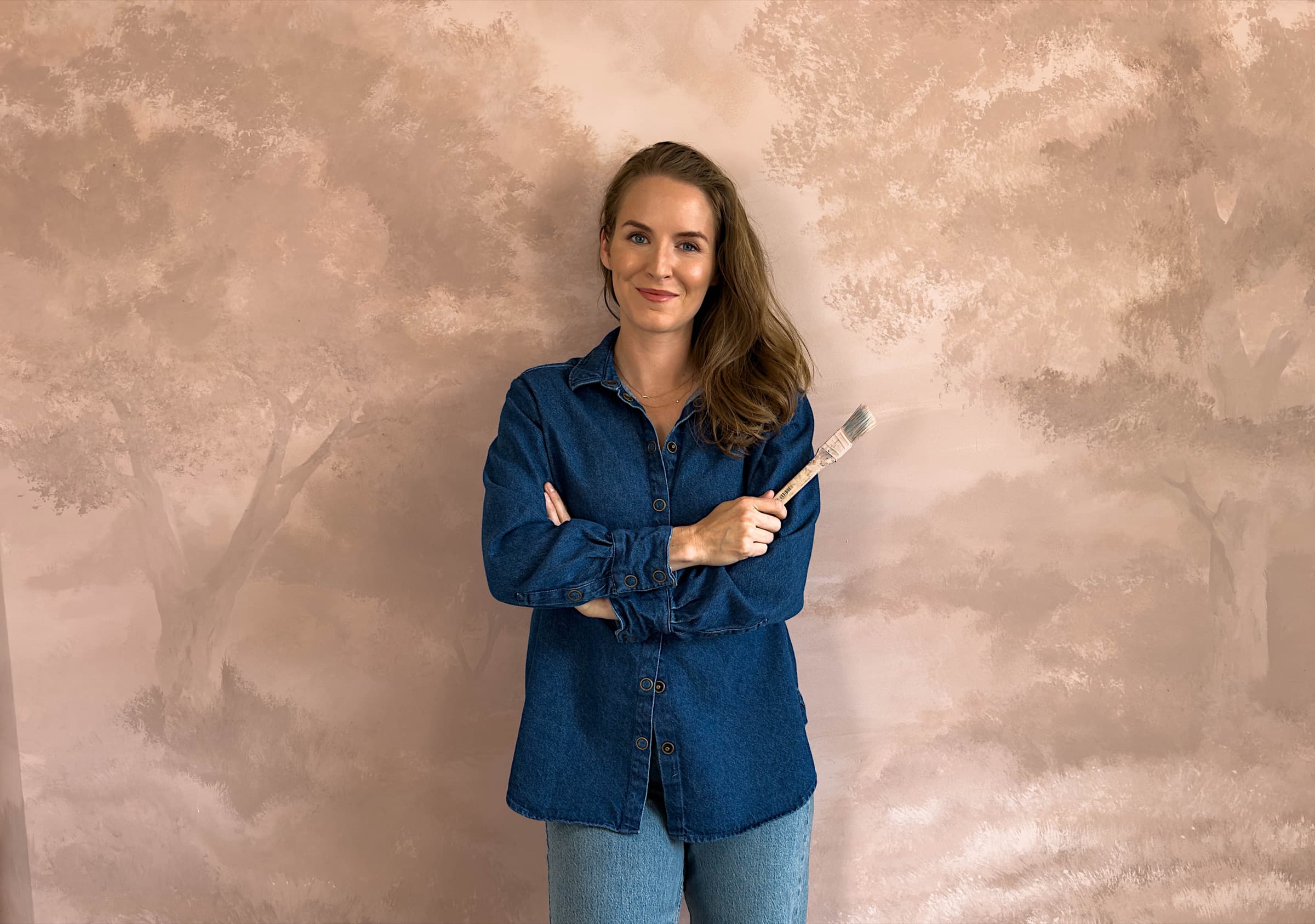 Anna standing beside a hand-painted sepia landscape mural in her studio.